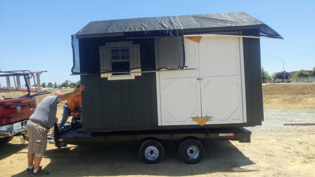 a green shed resting on a trailer towed by a truck