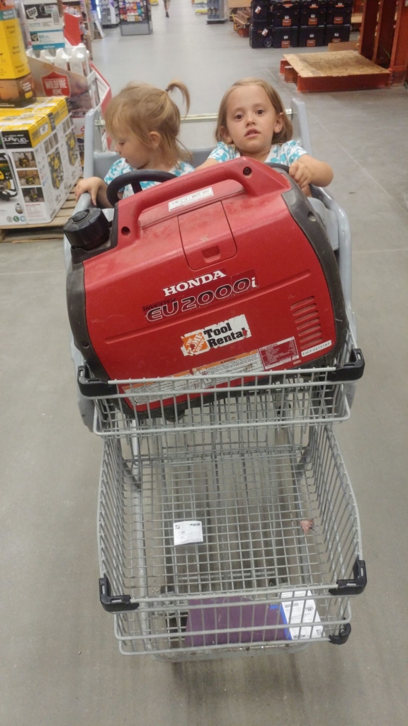 Two girls in a shopping cart with a large red generator in front of them