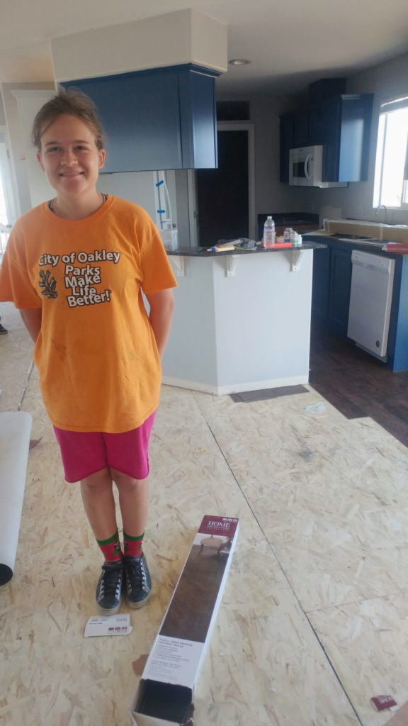 A teenager in an orange shirt standing in a partially finished kitchen