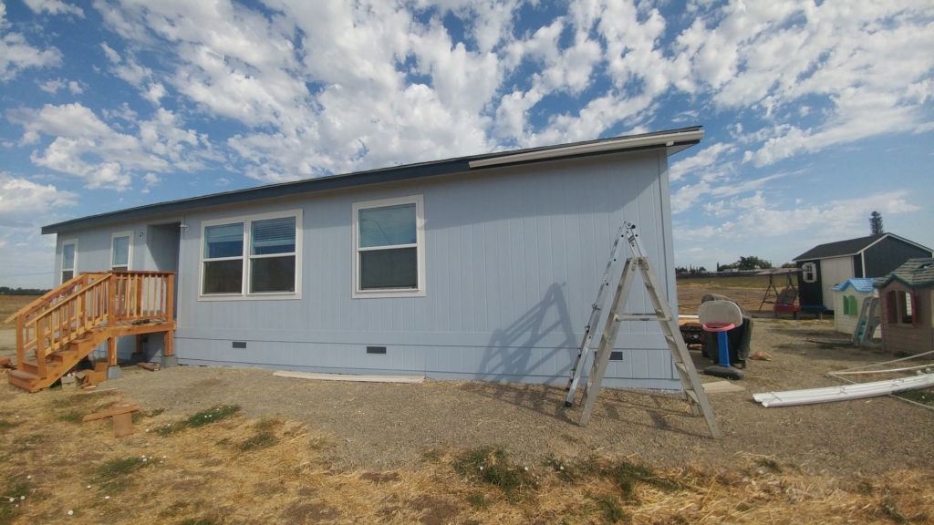 a home in the country with ladders next to partial vinyl gutters