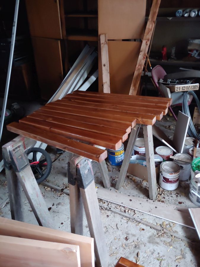 stained wood on a sawhorses with some junk in the background